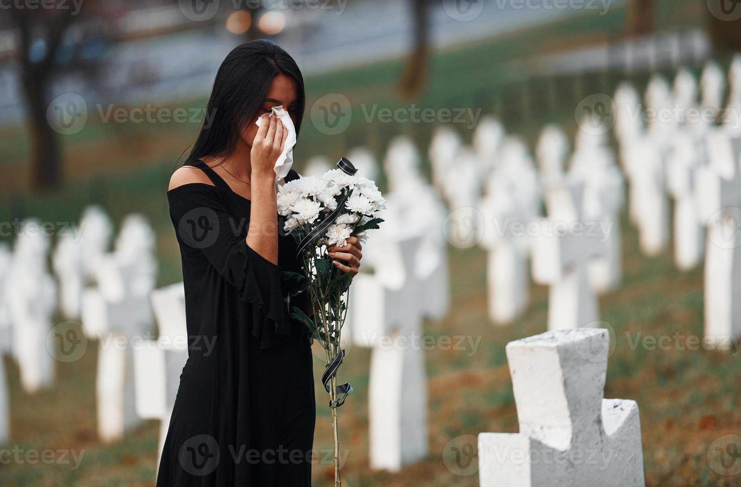 Young woman in black clothes visiting cemetery with many white crosses. Conception of funeral and death photo