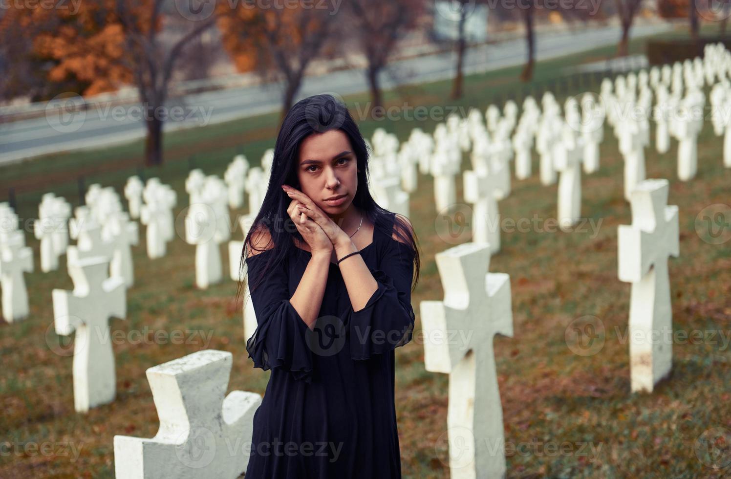 Young woman in black clothes visiting cemetery with many white crosses. Conception of funeral and death photo