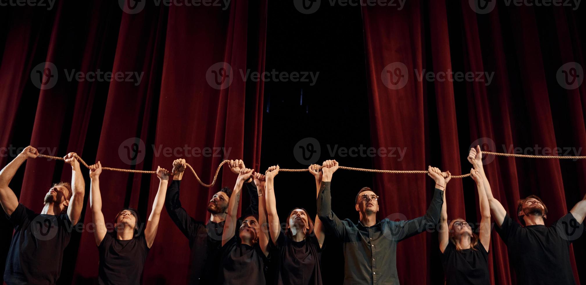 Holding rope in hands above the heads. Group of actors in dark colored clothes on rehearsal in the theater photo