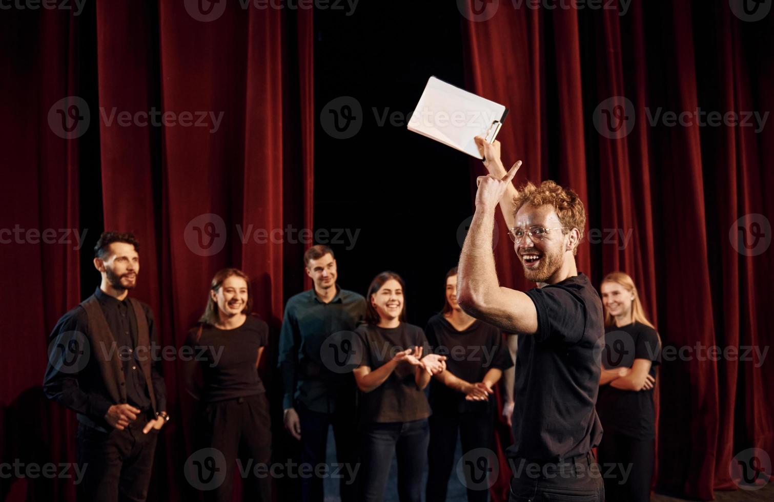 Man with notepad practice his role. Group of actors in dark colored clothes on rehearsal in the theater photo