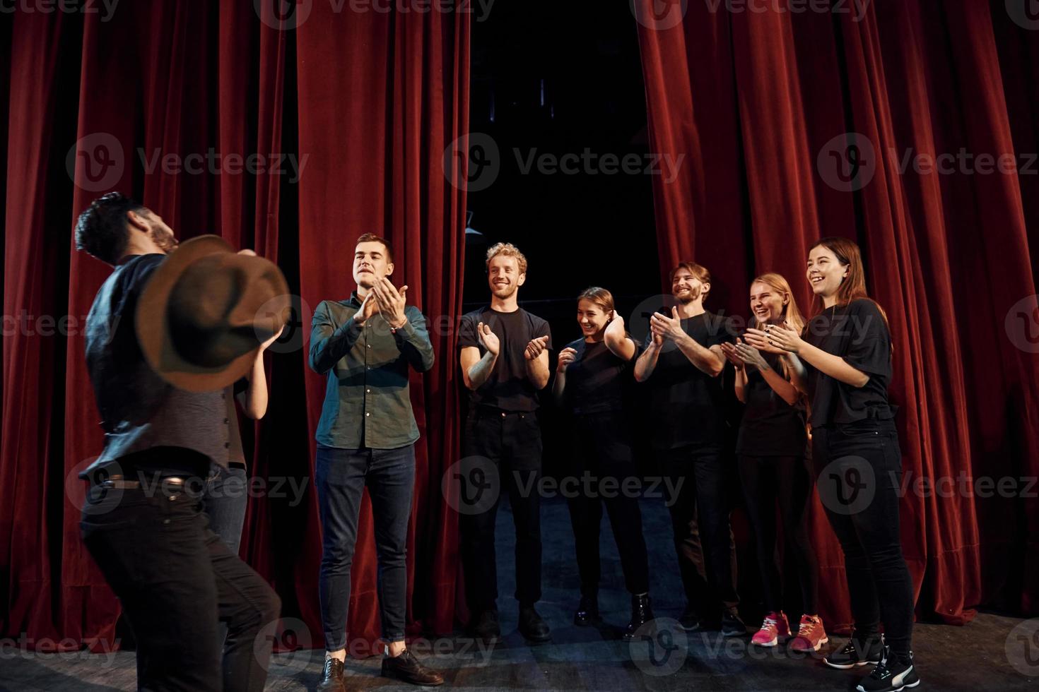 Standing against red curtains. Group of actors in dark colored clothes on rehearsal in the theater photo