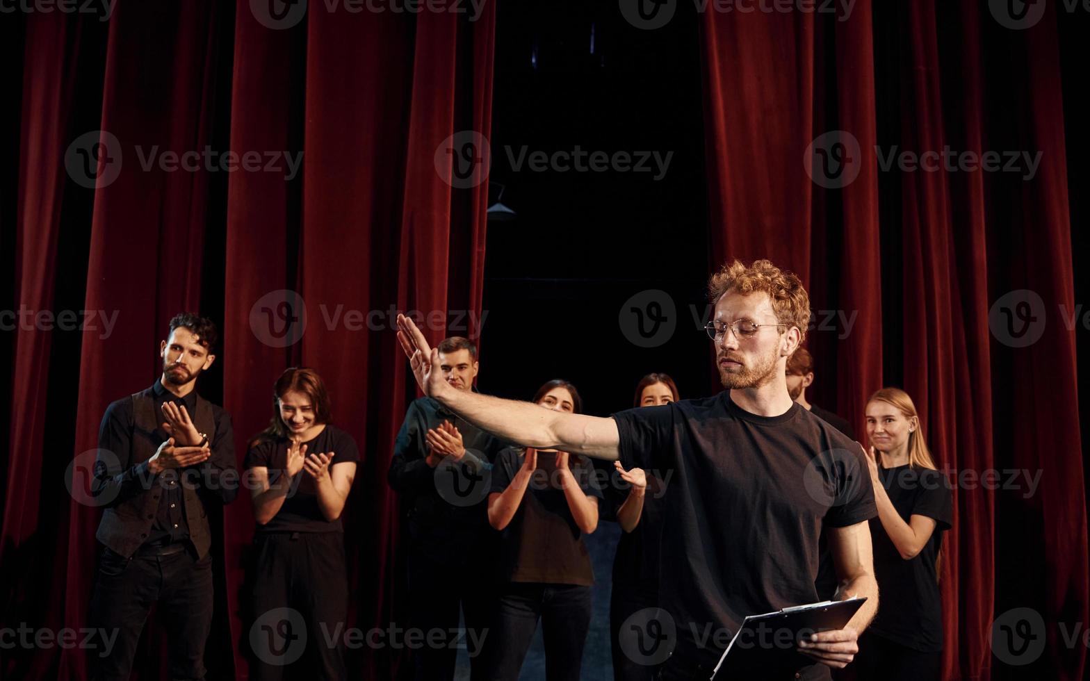 Man with notepad practice his role. Group of actors in dark colored clothes on rehearsal in the theater photo