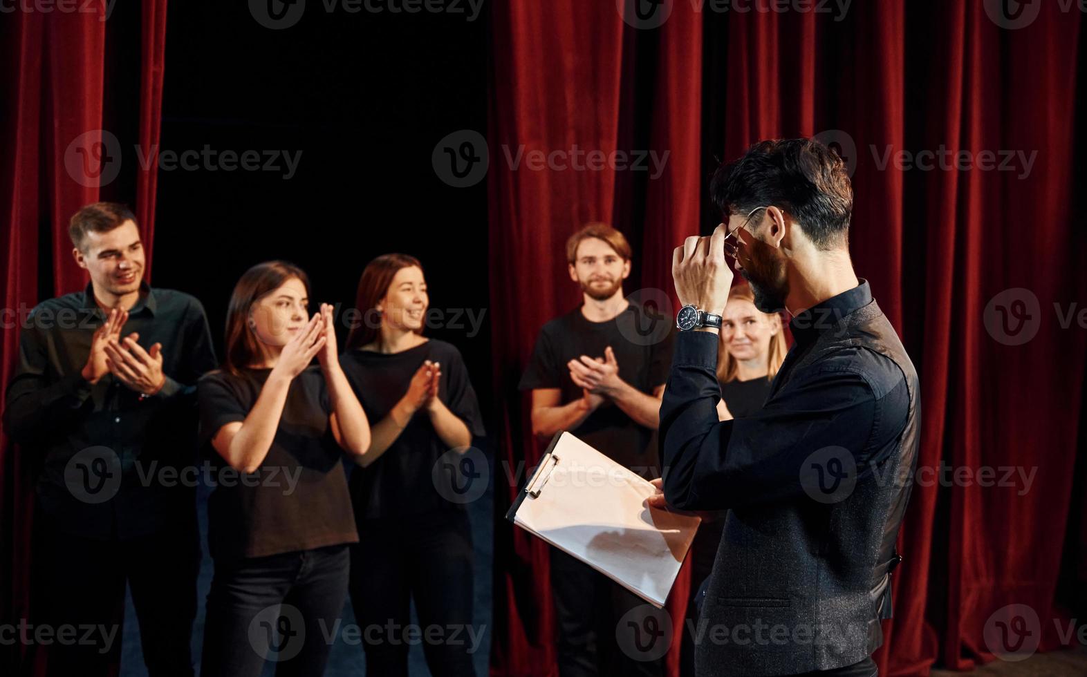 chico expresionable practicando su papel. grupo de actores con ropa de color oscuro ensayando en el teatro foto