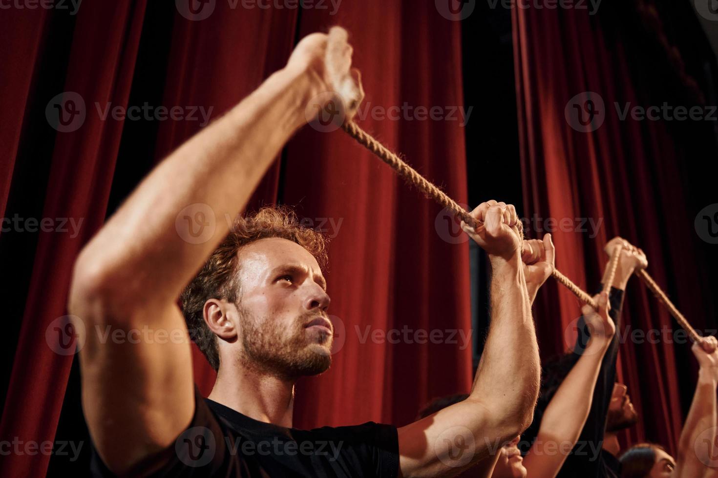 Holding rope in hands above the heads. Group of actors in dark colored clothes on rehearsal in the theater photo