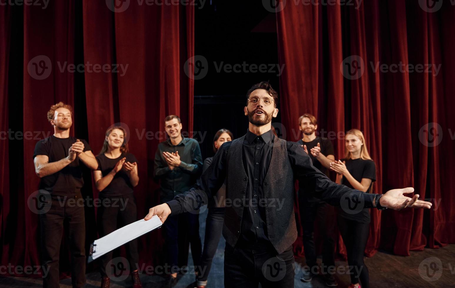 chico expresionable practicando su papel. grupo de actores con ropa de color oscuro ensayando en el teatro foto