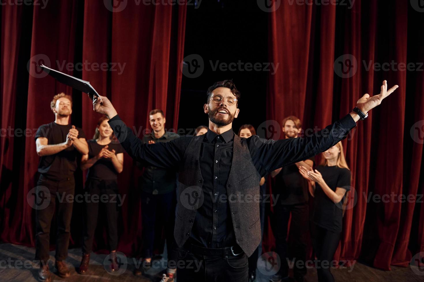 Expressionalible guy practicing his role. Group of actors in dark colored clothes on rehearsal in the theater photo