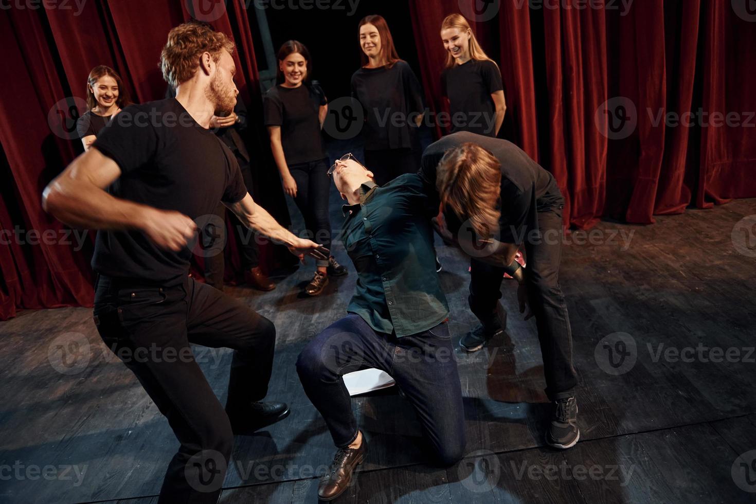 escena de lucha. grupo de actores con ropa de color oscuro ensayando en el teatro foto