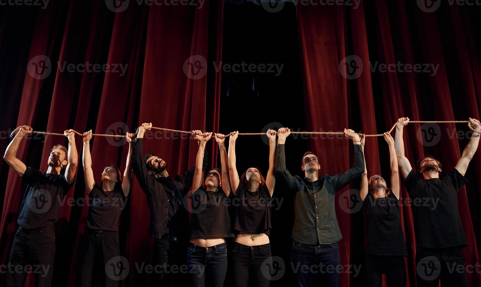 sosteniendo la cuerda en las manos por encima de la cabeza. grupo de actores con ropa de color oscuro ensayando en el teatro foto