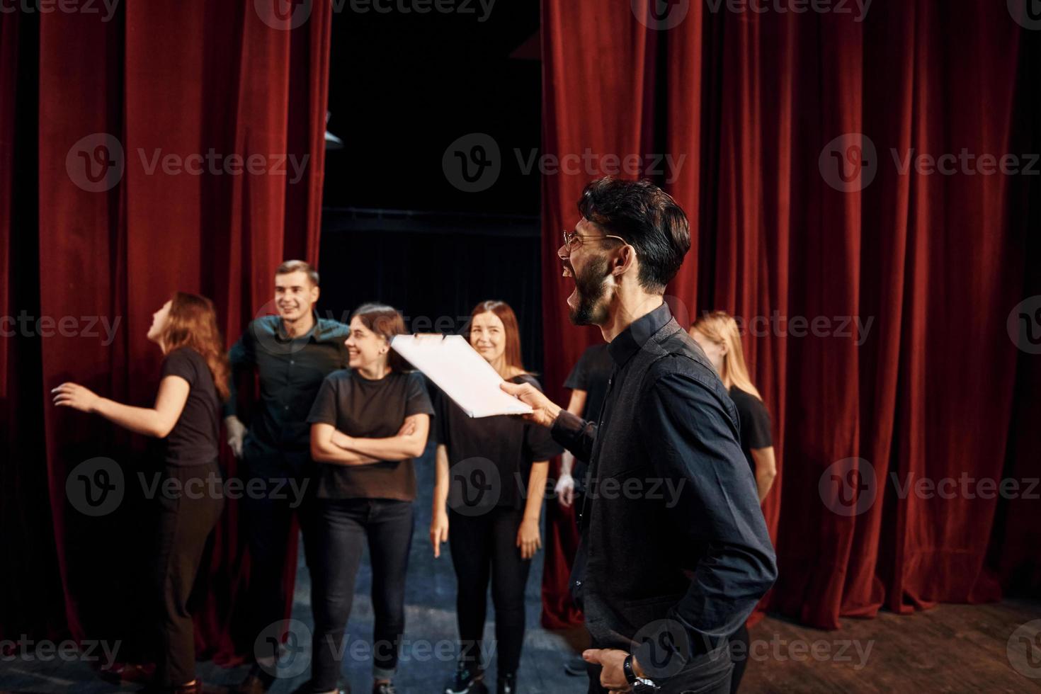 chico expresionable practicando su papel. grupo de actores con ropa de color oscuro ensayando en el teatro foto