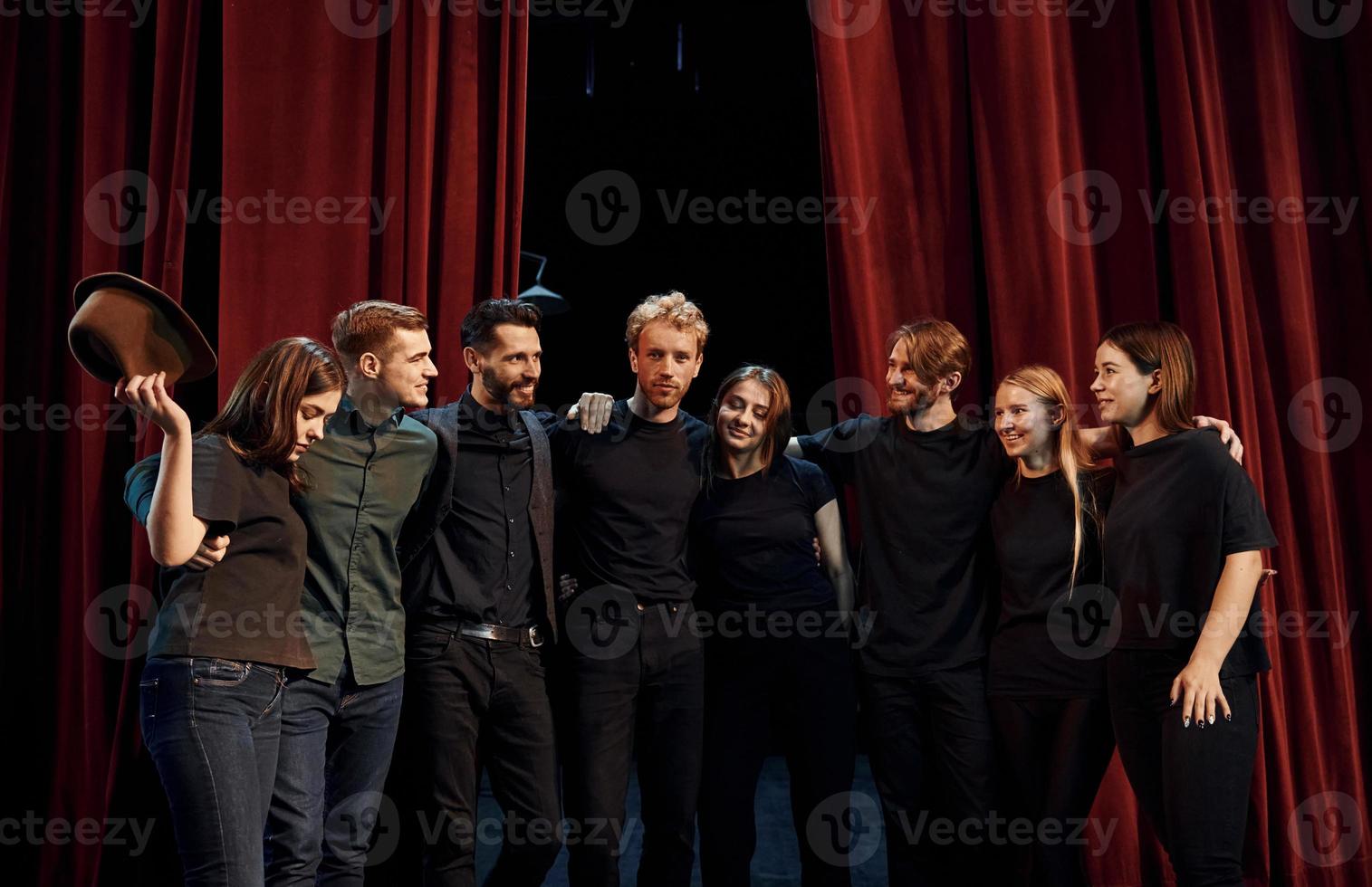 Standing against red curtains. Group of actors in dark colored clothes on rehearsal in the theater photo