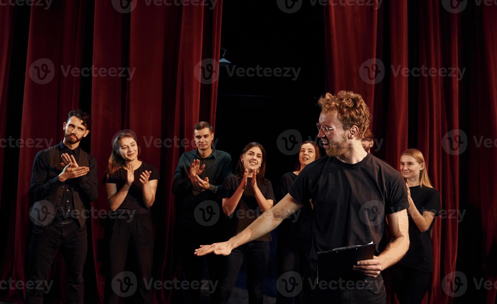 Man with notepad practice his role. Group of actors in dark colored clothes on rehearsal in the theater photo