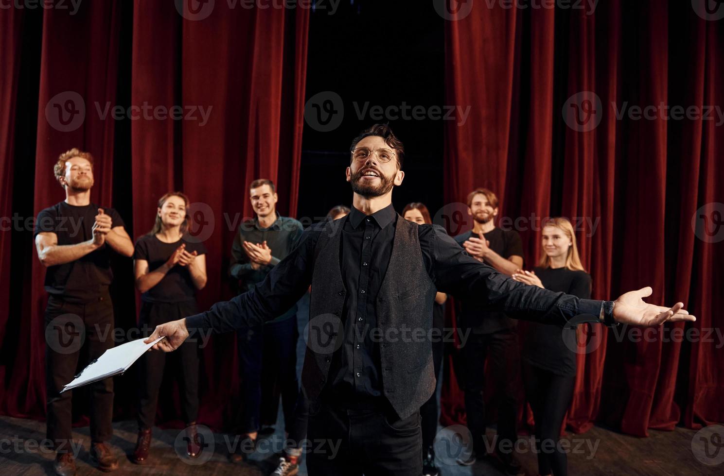 Expressionalible guy practicing his role. Group of actors in dark colored clothes on rehearsal in the theater photo