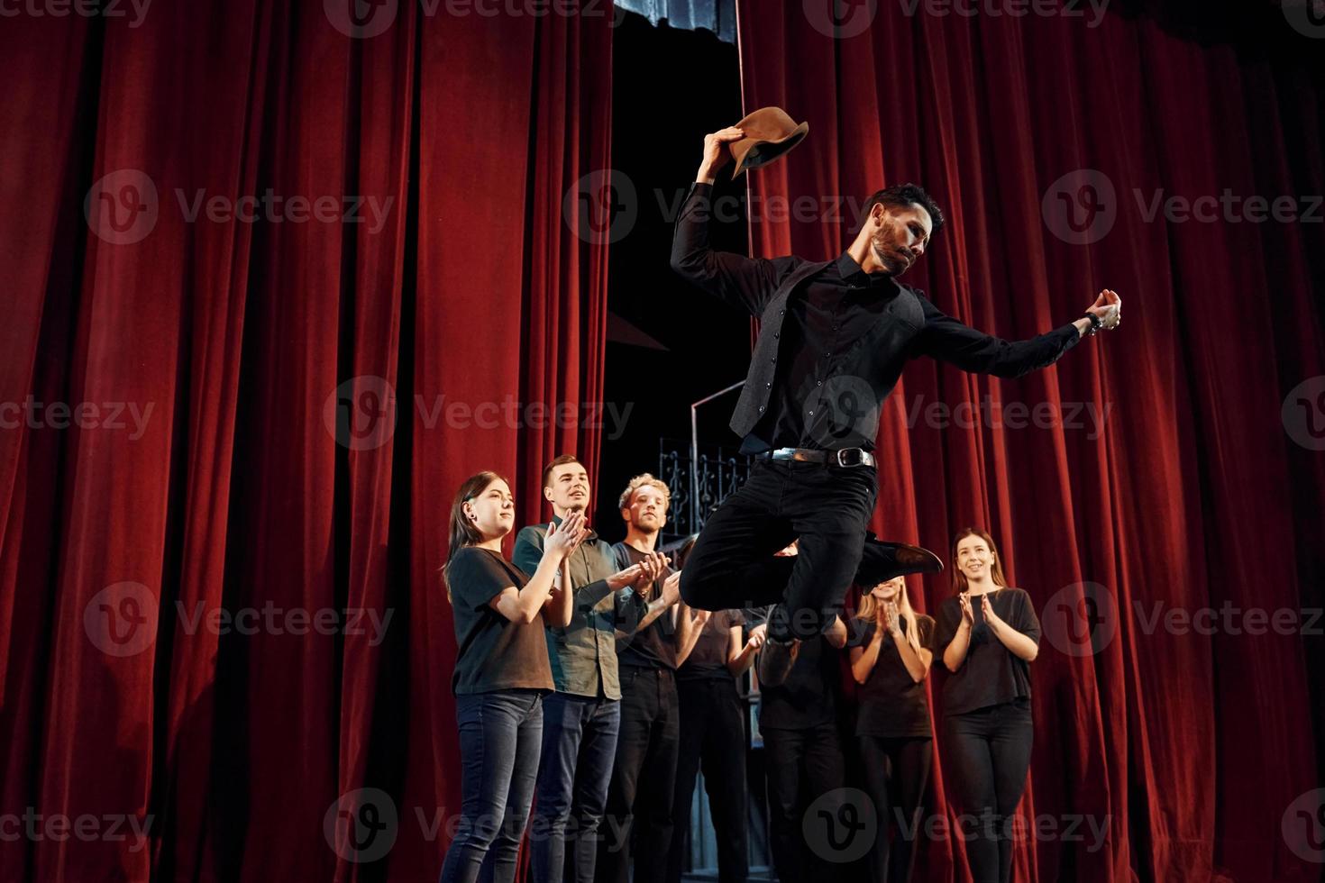 Standing against red curtains. Group of actors in dark colored clothes on rehearsal in the theater photo