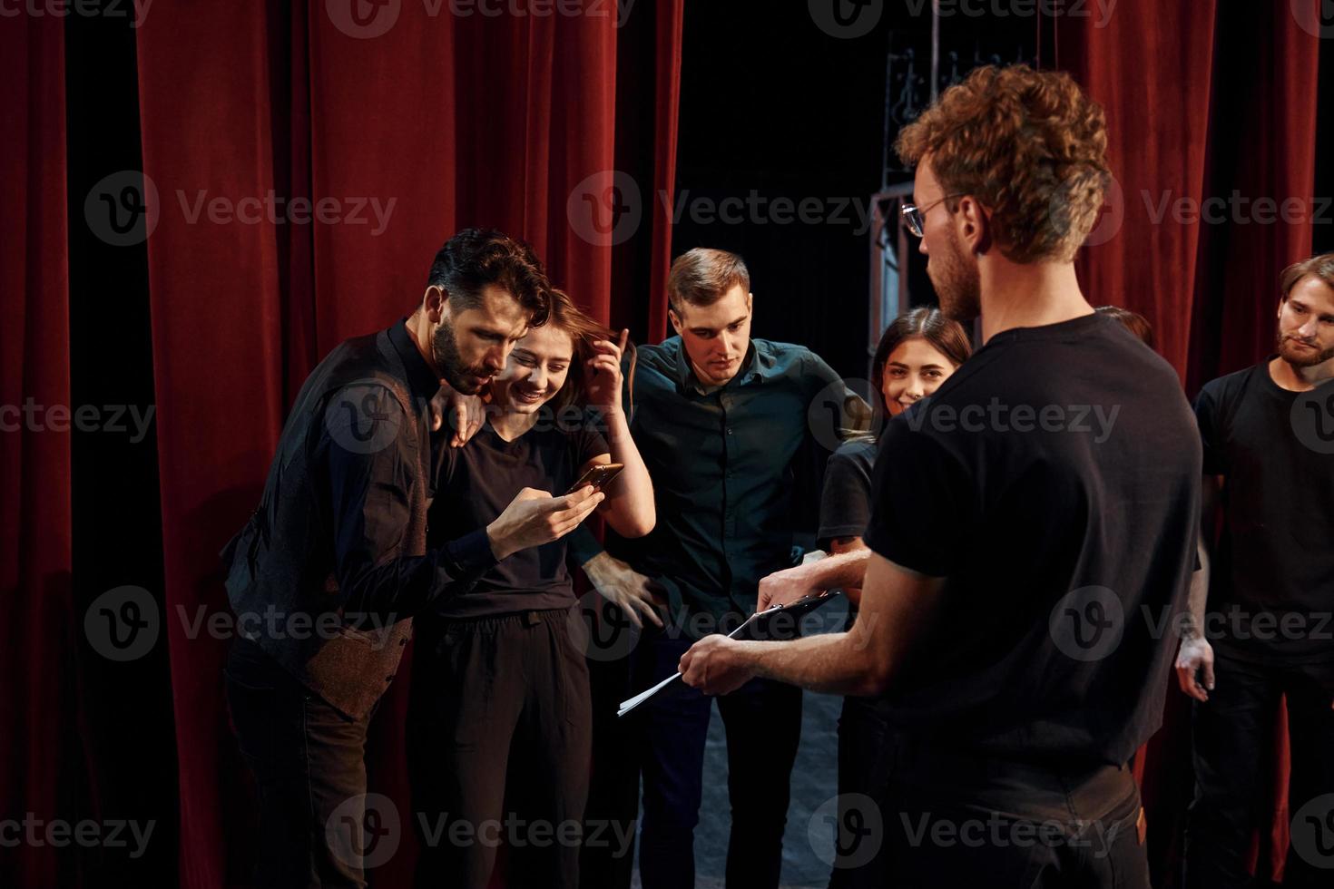 Man with notepad practice his role. Group of actors in dark colored clothes on rehearsal in the theater photo