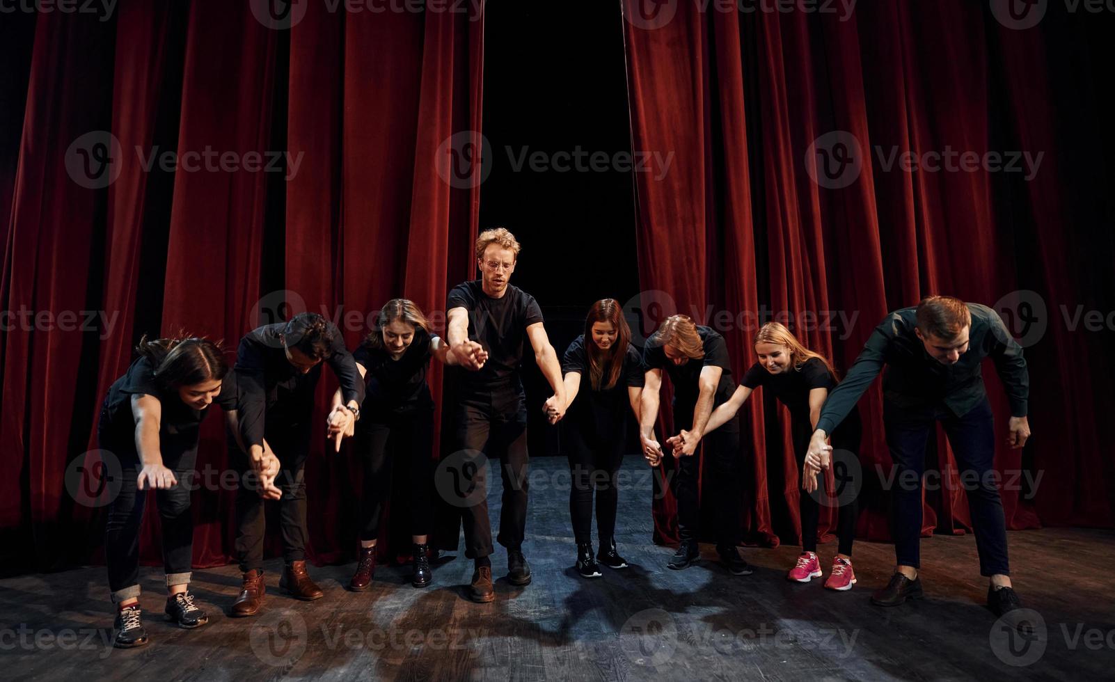 People bowing to audience. Group of actors in dark colored clothes on rehearsal in the theater photo