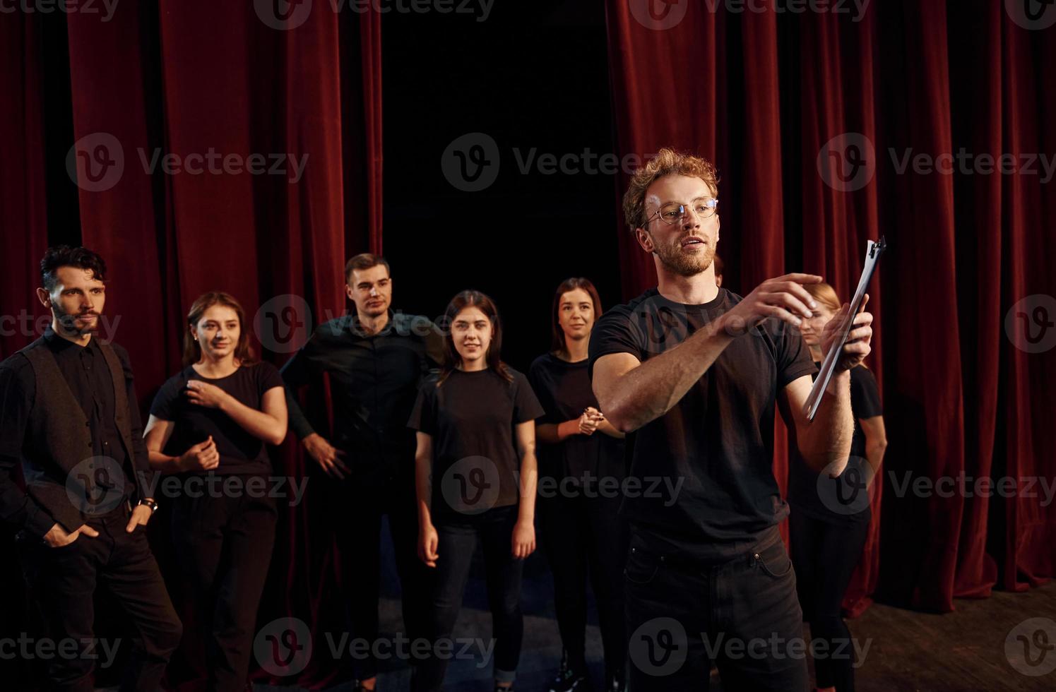 Man with notepad practice his role. Group of actors in dark colored clothes on rehearsal in the theater photo