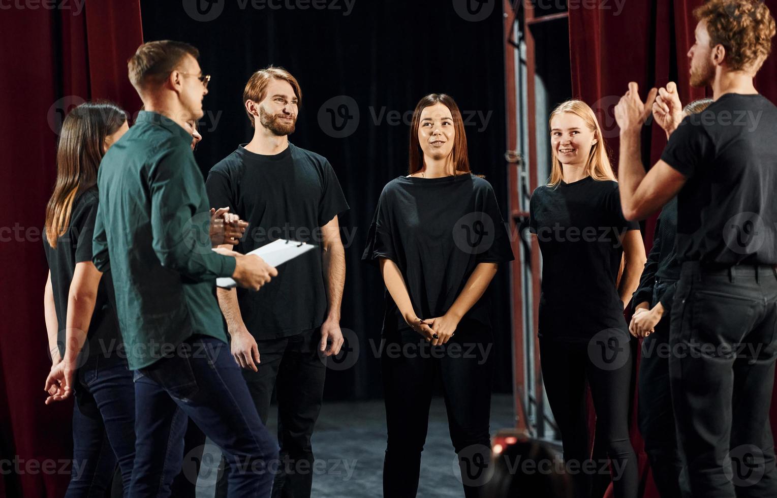 Standing against red curtains. Group of actors in dark colored clothes on rehearsal in the theater photo