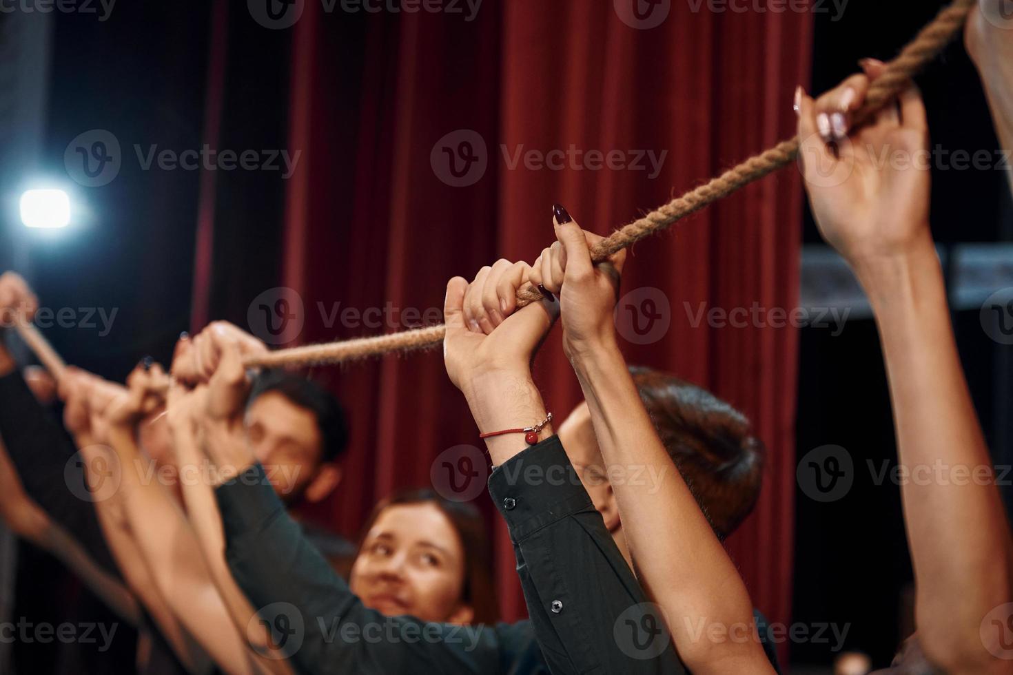 Holding rope in hands above the heads. Group of actors in dark colored clothes on rehearsal in the theater photo