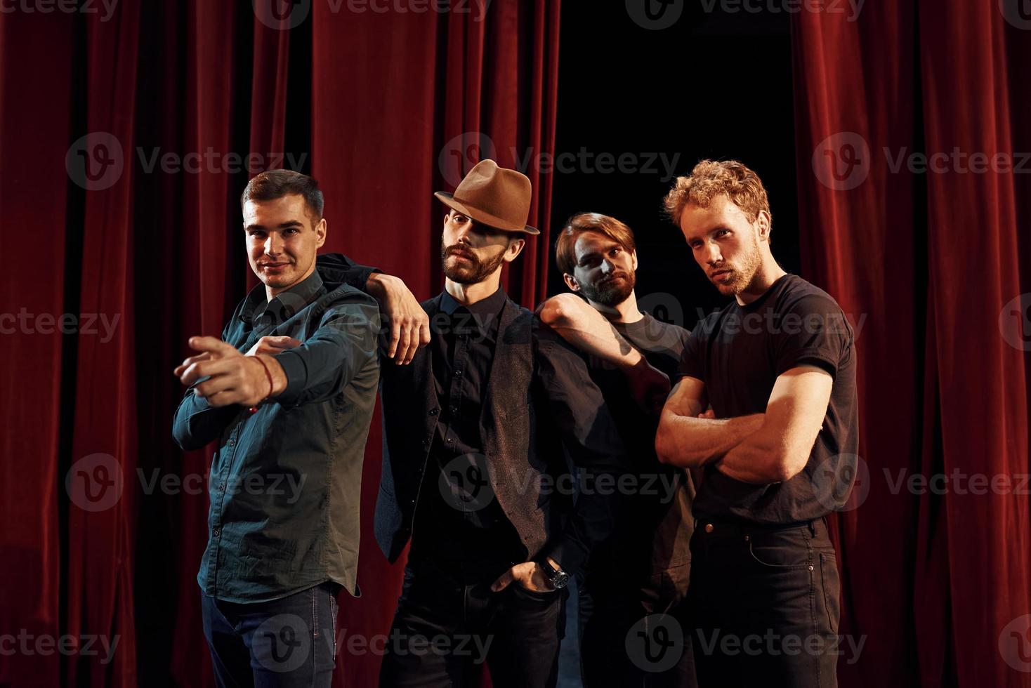 de pie contra las cortinas rojas. grupo de actores con ropa de color oscuro ensayando en el teatro foto