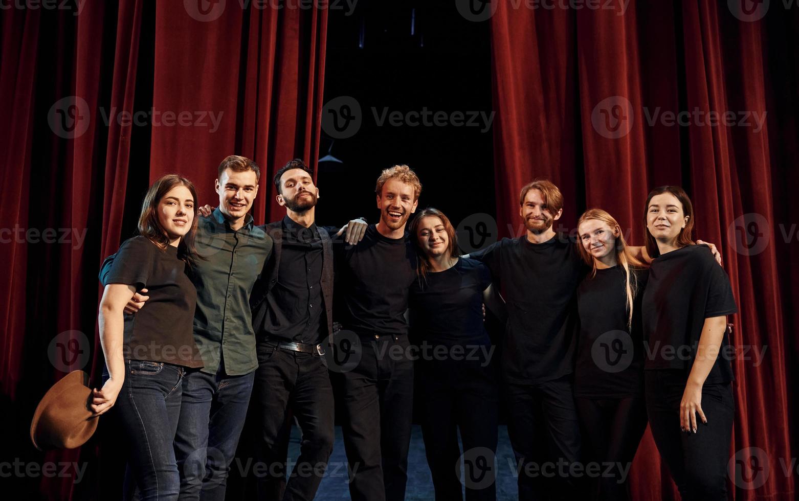 Standing against red curtains. Group of actors in dark colored clothes on rehearsal in the theater photo