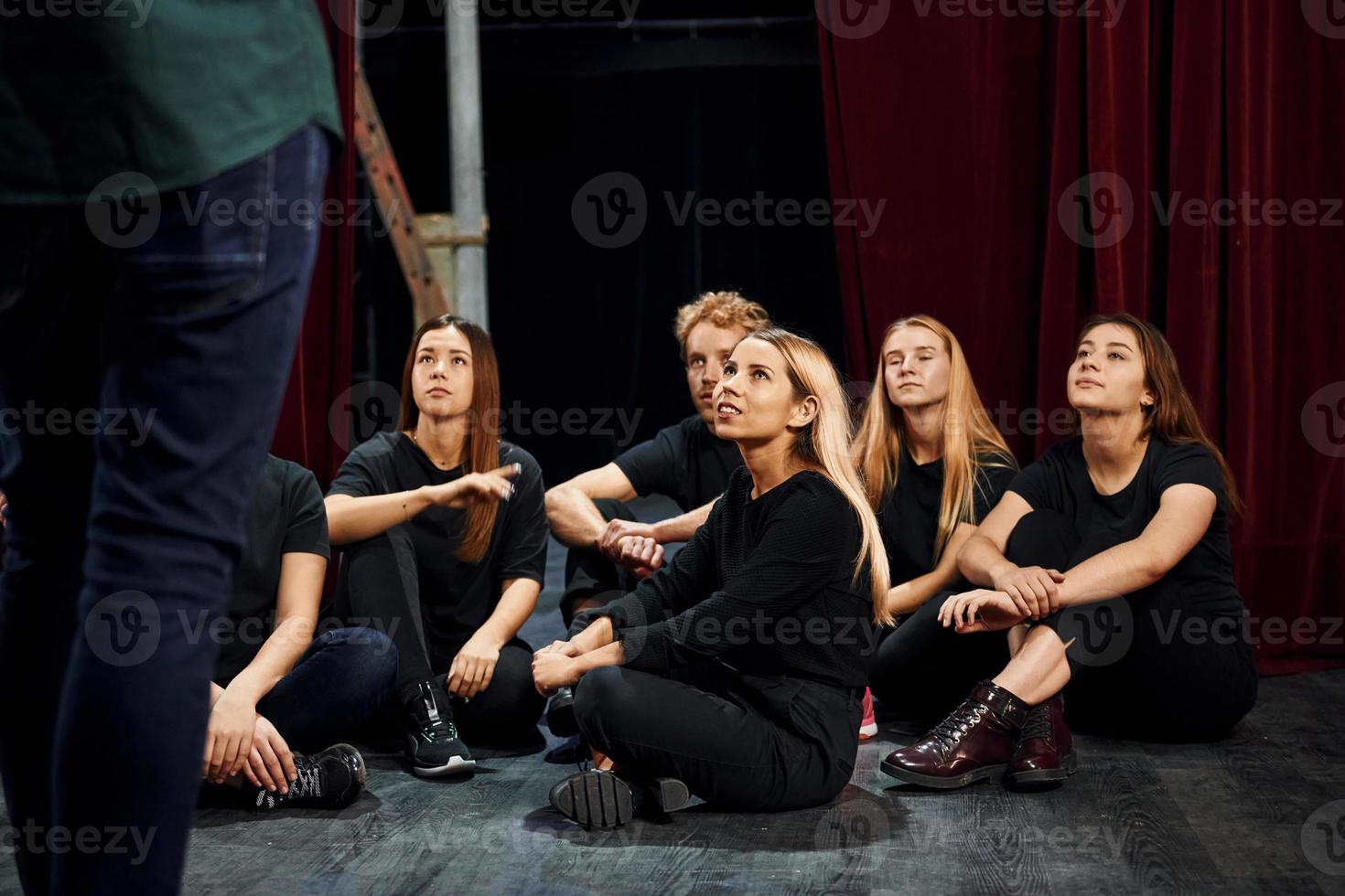 Sitting and listening to man. Group of actors in dark colored clothes on rehearsal in the theater photo