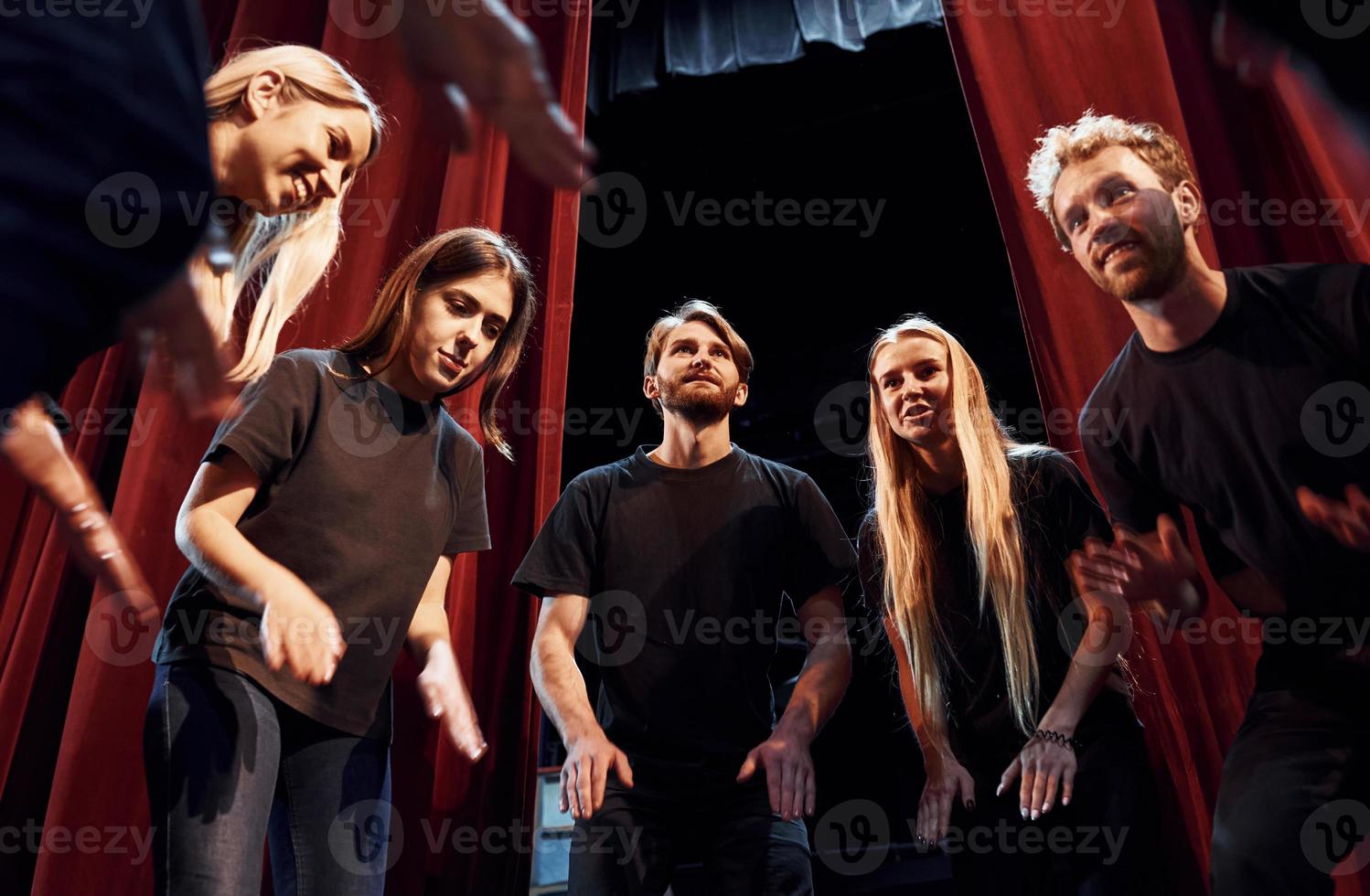 Standing against red curtains. Group of actors in dark colored clothes on rehearsal in the theater photo