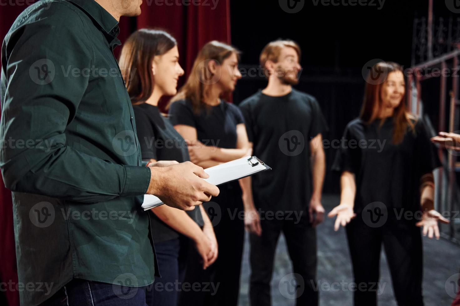 Standing against red curtains. Group of actors in dark colored clothes on rehearsal in the theater photo