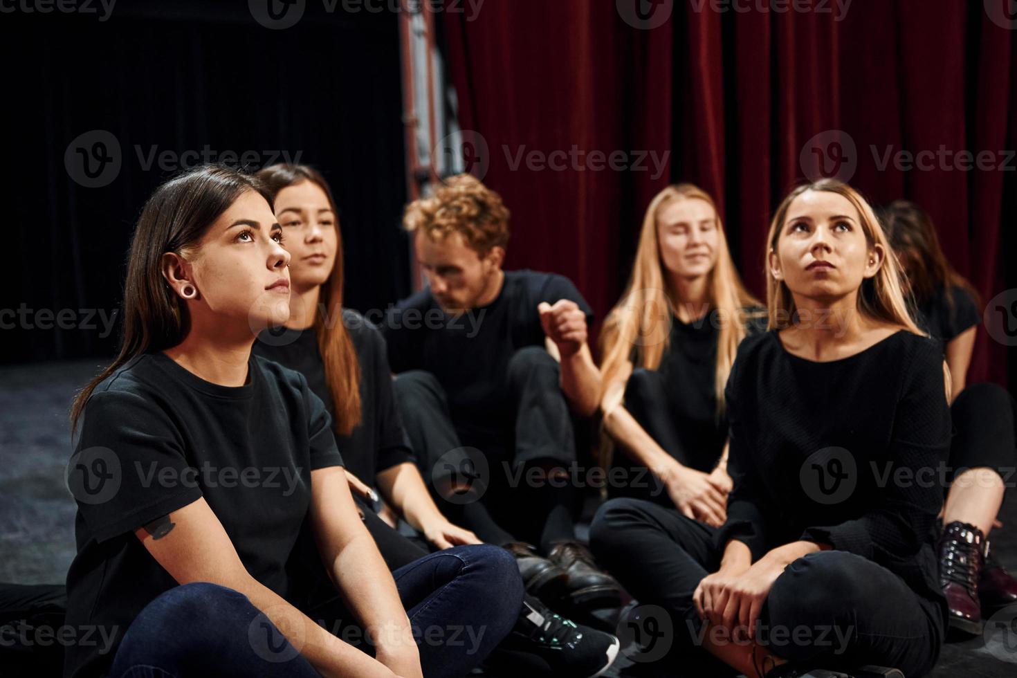 Sitting on the floor. Group of actors in dark colored clothes on rehearsal in the theater photo