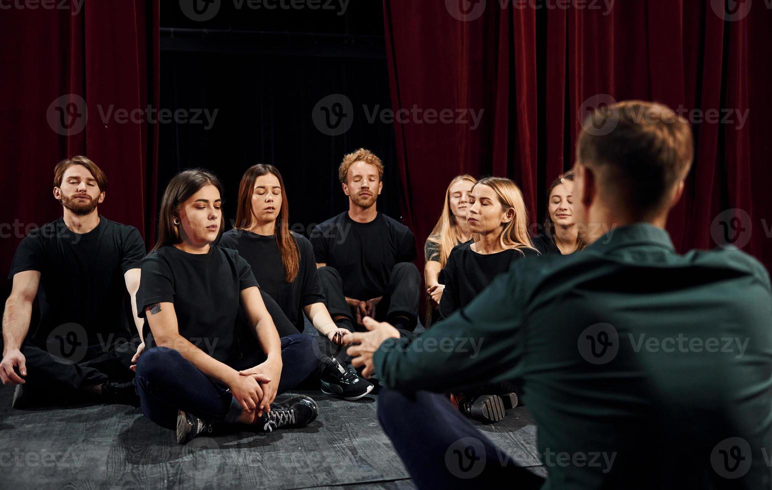 Sitting on the floor. Group of actors in dark colored clothes on rehearsal in the theater photo