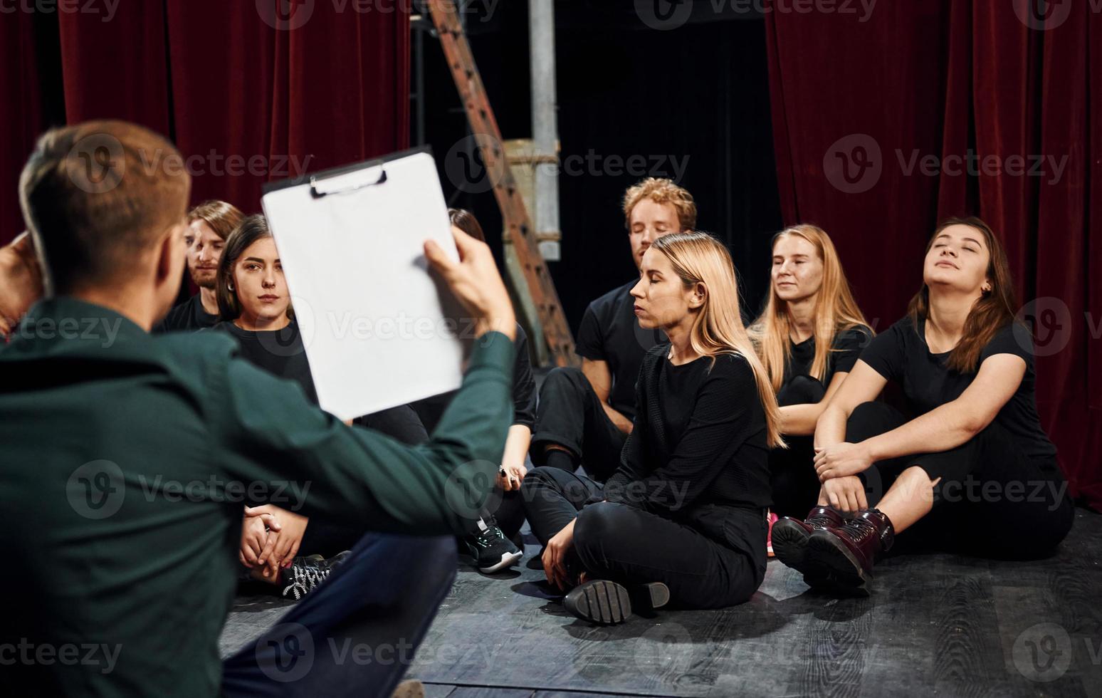 Sitting on the floor. Group of actors in dark colored clothes on rehearsal in the theater photo