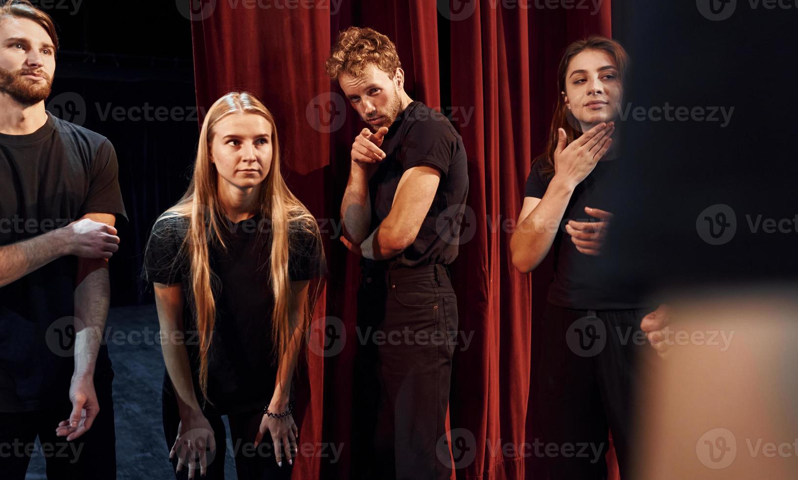 Standing against red curtains. Group of actors in dark colored clothes on rehearsal in the theater photo