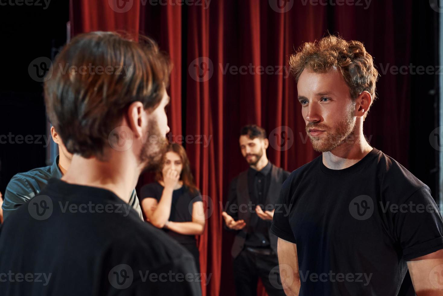 Two people talking. Group of actors in dark colored clothes on rehearsal in the theater photo