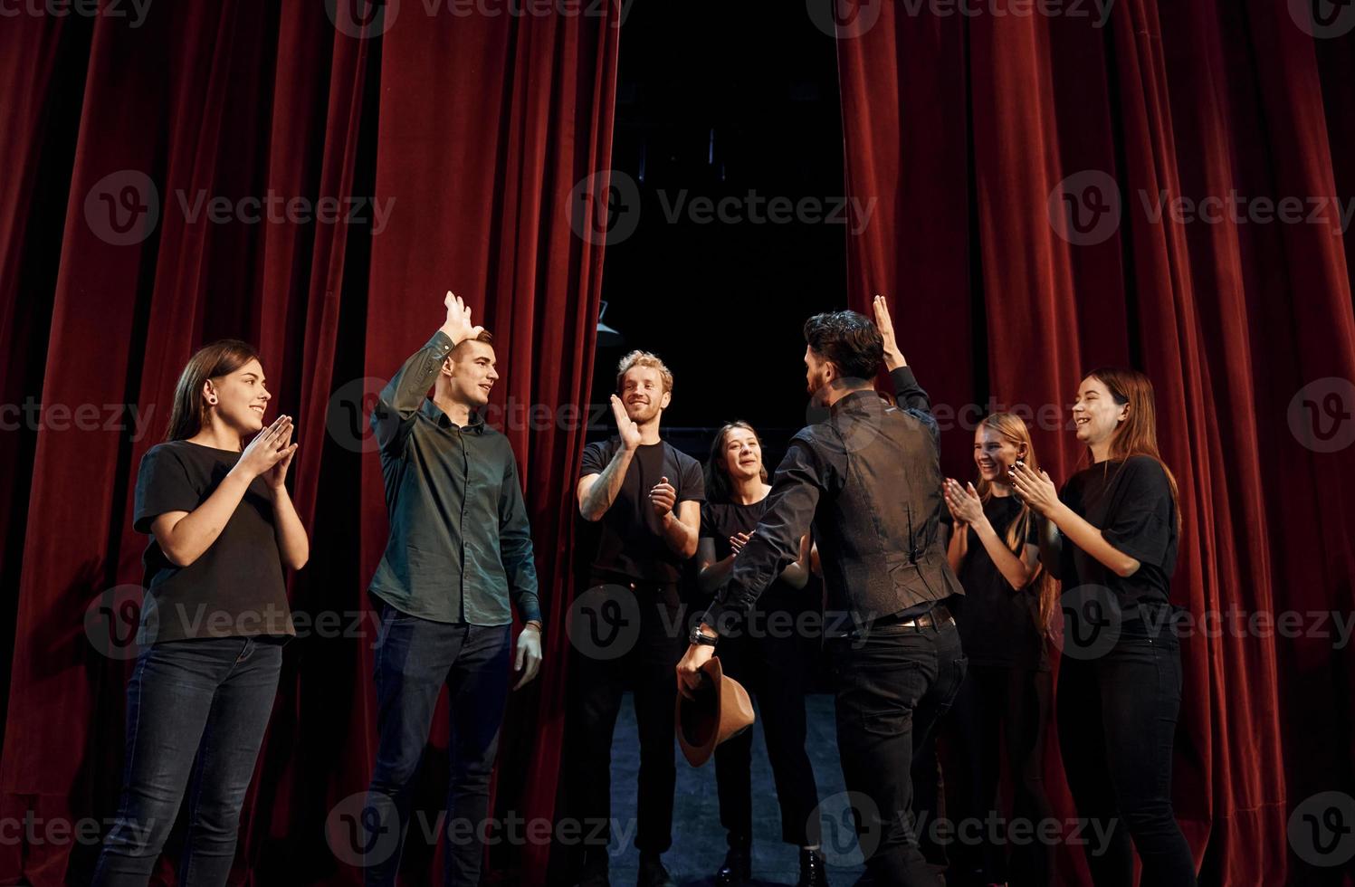 Standing against red curtains. Group of actors in dark colored clothes on rehearsal in the theater photo