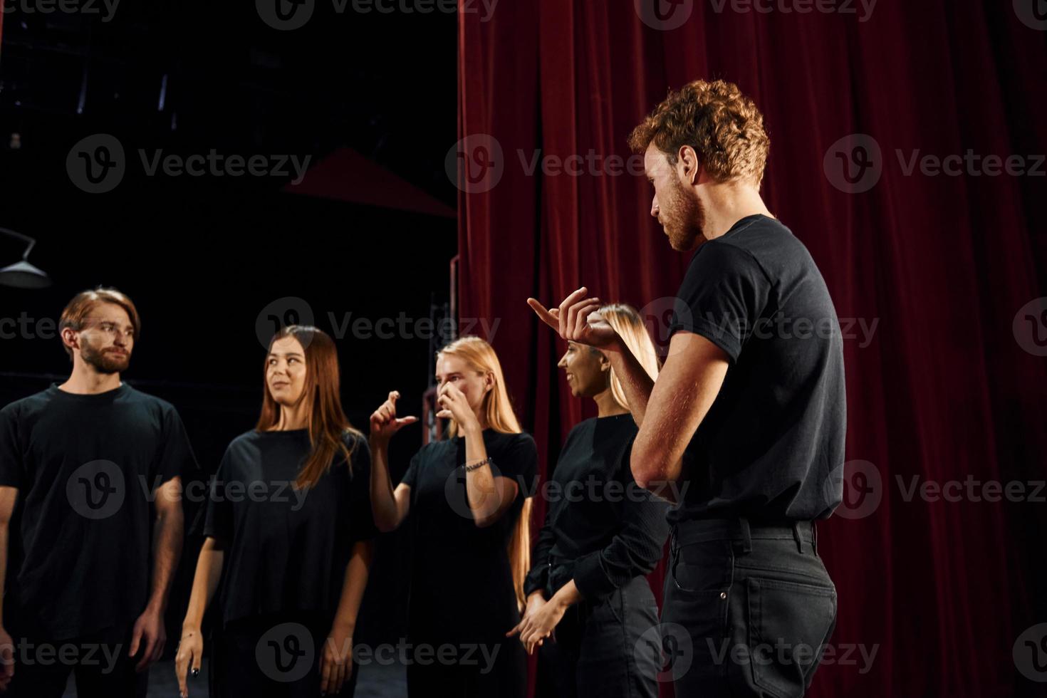 Standing against red curtains. Group of actors in dark colored clothes on rehearsal in the theater photo