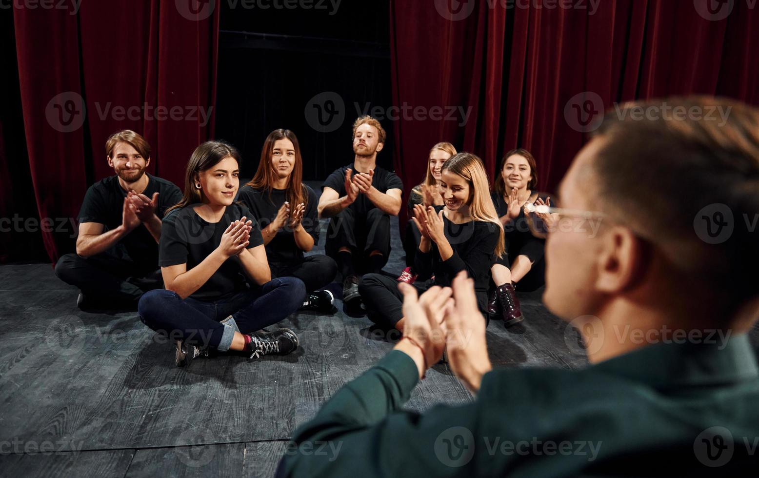 Sitting on the floor. Group of actors in dark colored clothes on rehearsal in the theater photo