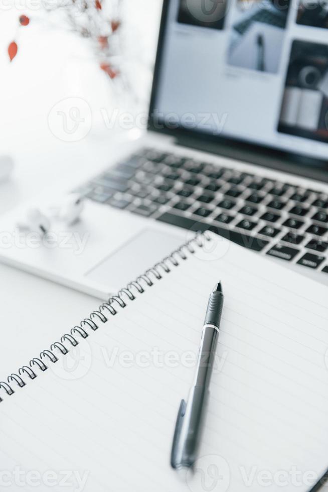 Close up view of notepad with pen on it and laptop at background photo