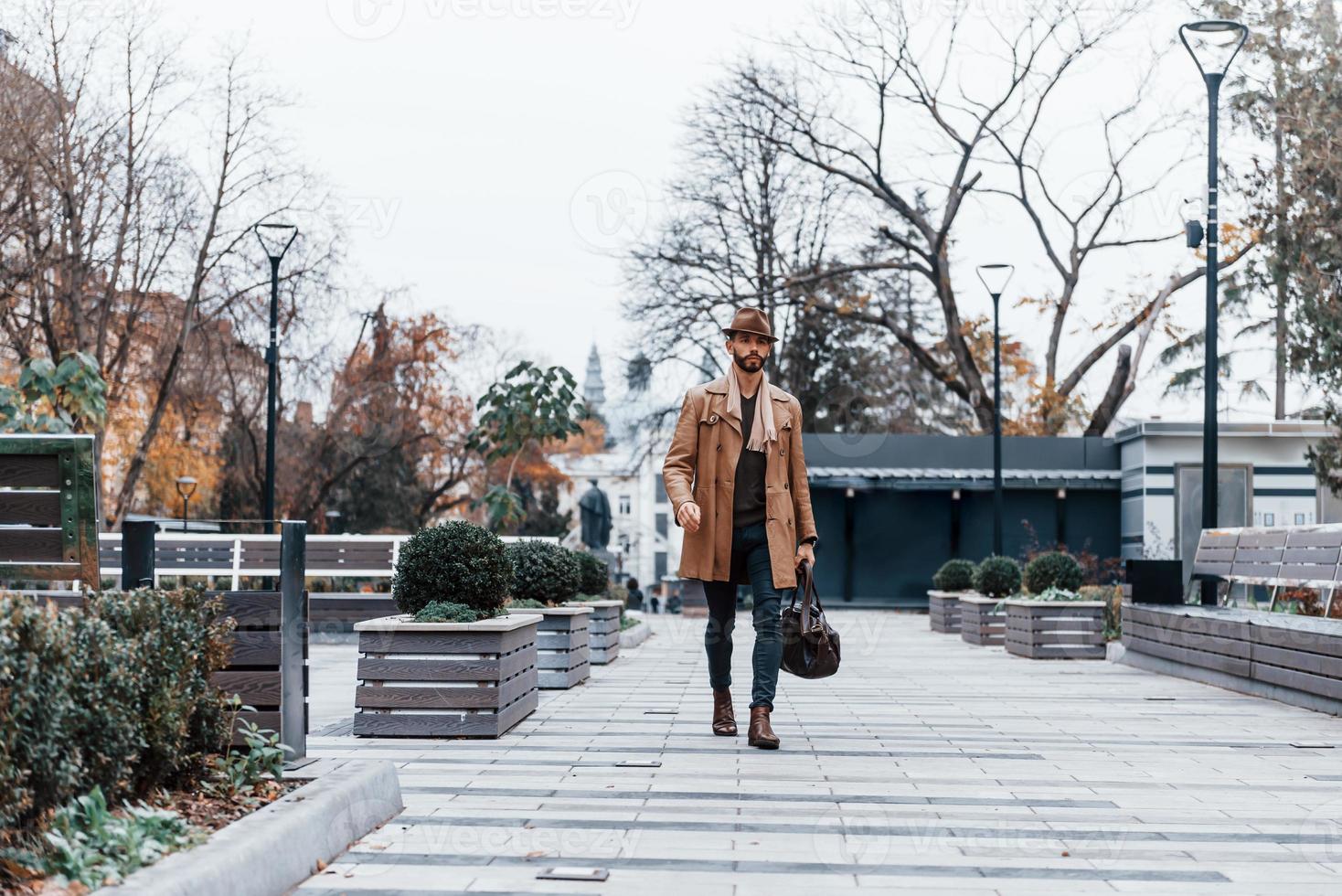 With bag. Young male model in fashionable clothes is outdoors in the city at daytime photo