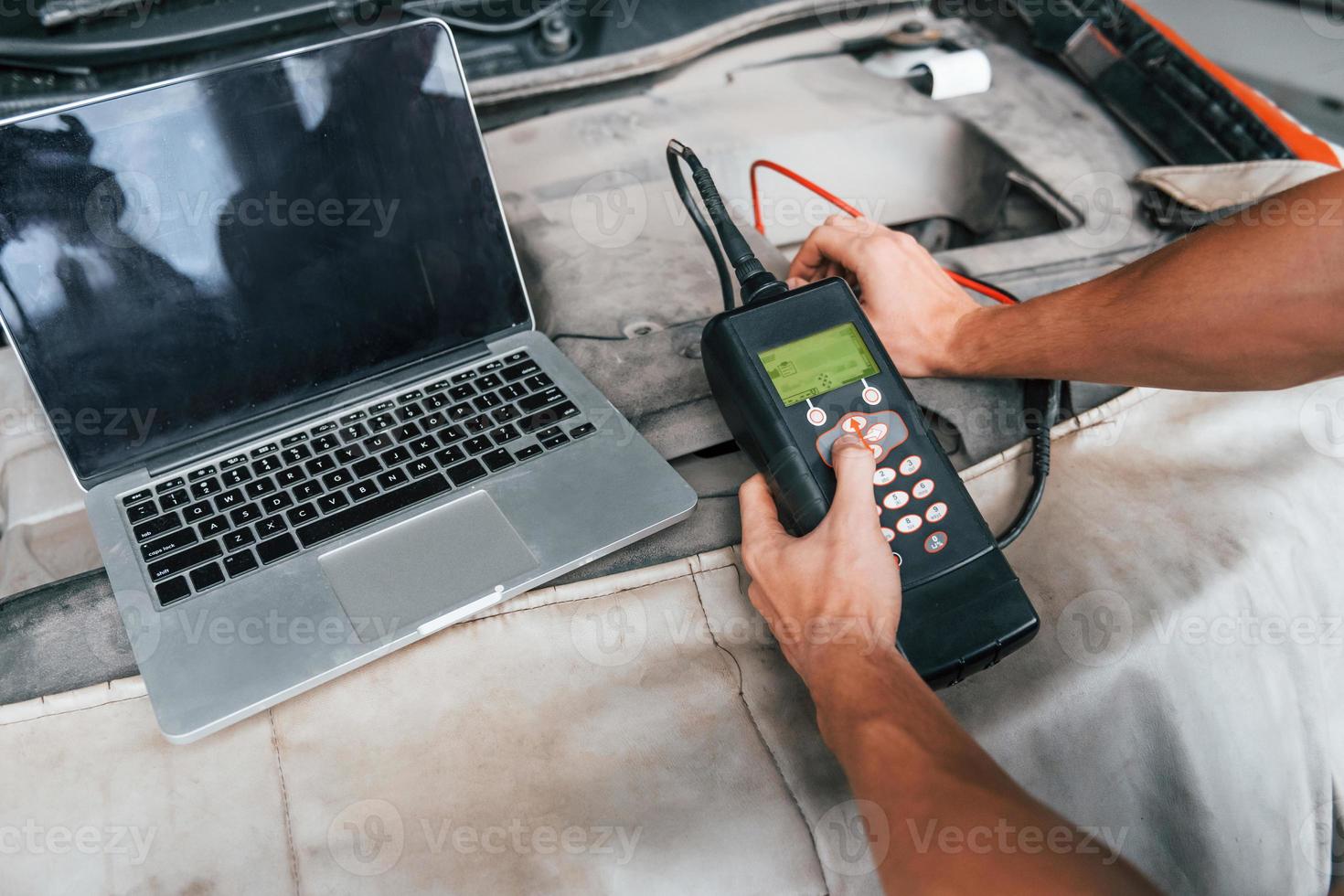 Close up view of man's hands that holding device for testing automobile in salon photo