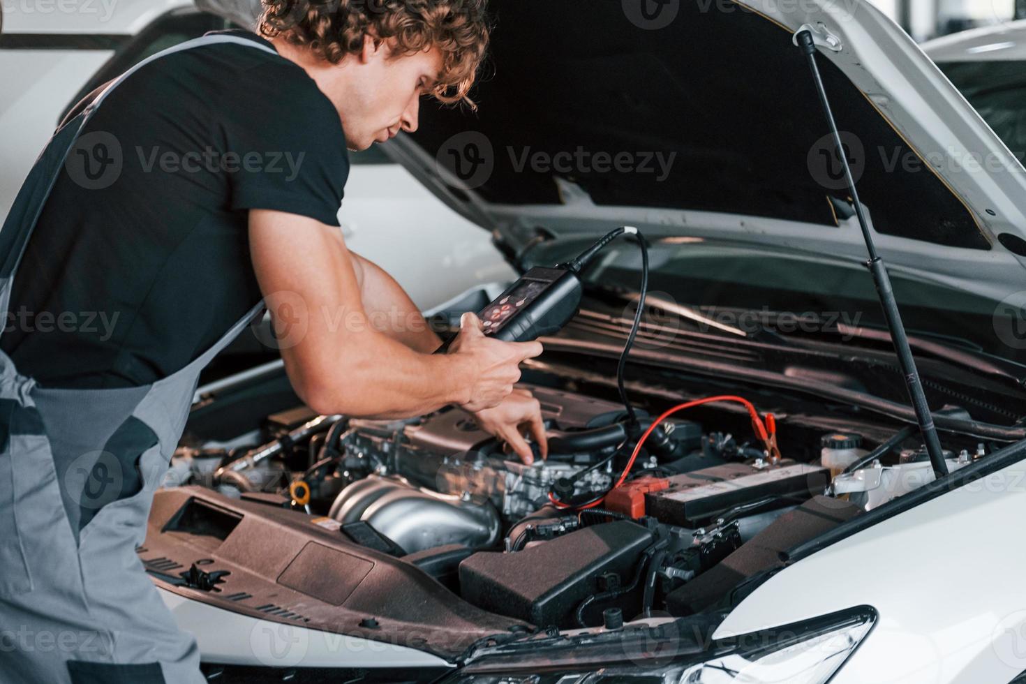 Tests car's electronics. Adult man in grey colored uniform works in the automobile salon photo