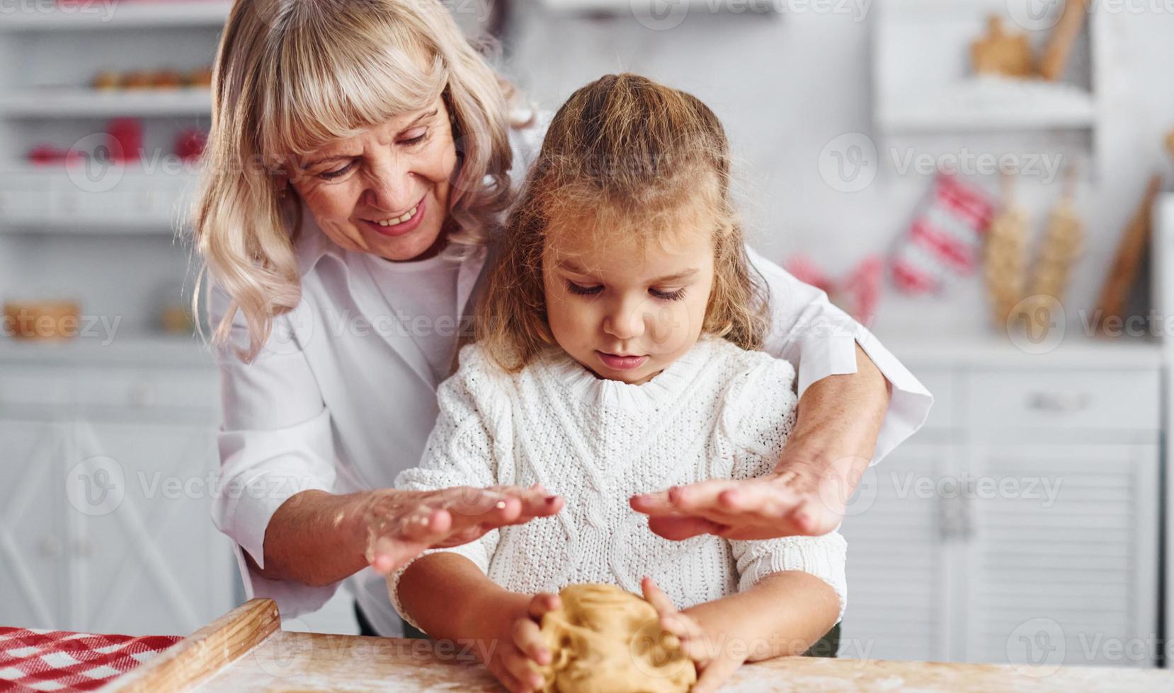 Kneads the dough. Senior grandmother with her little granddaughter cooks sweets for Christmas on the kitchen photo