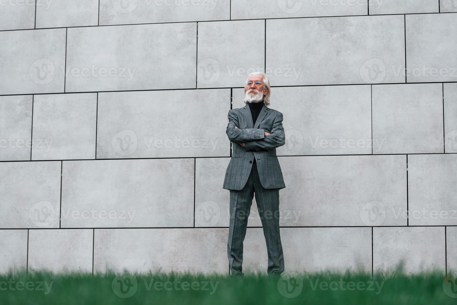 un hombre de negocios de alto rango vestido con ropa formal, con cabello gris y barba, está al aire libre parado contra la pared foto