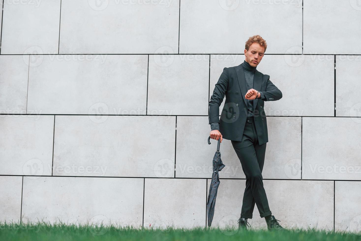 Young man in formal clothes with umbrella standing near wall outdoors with umbrella photo