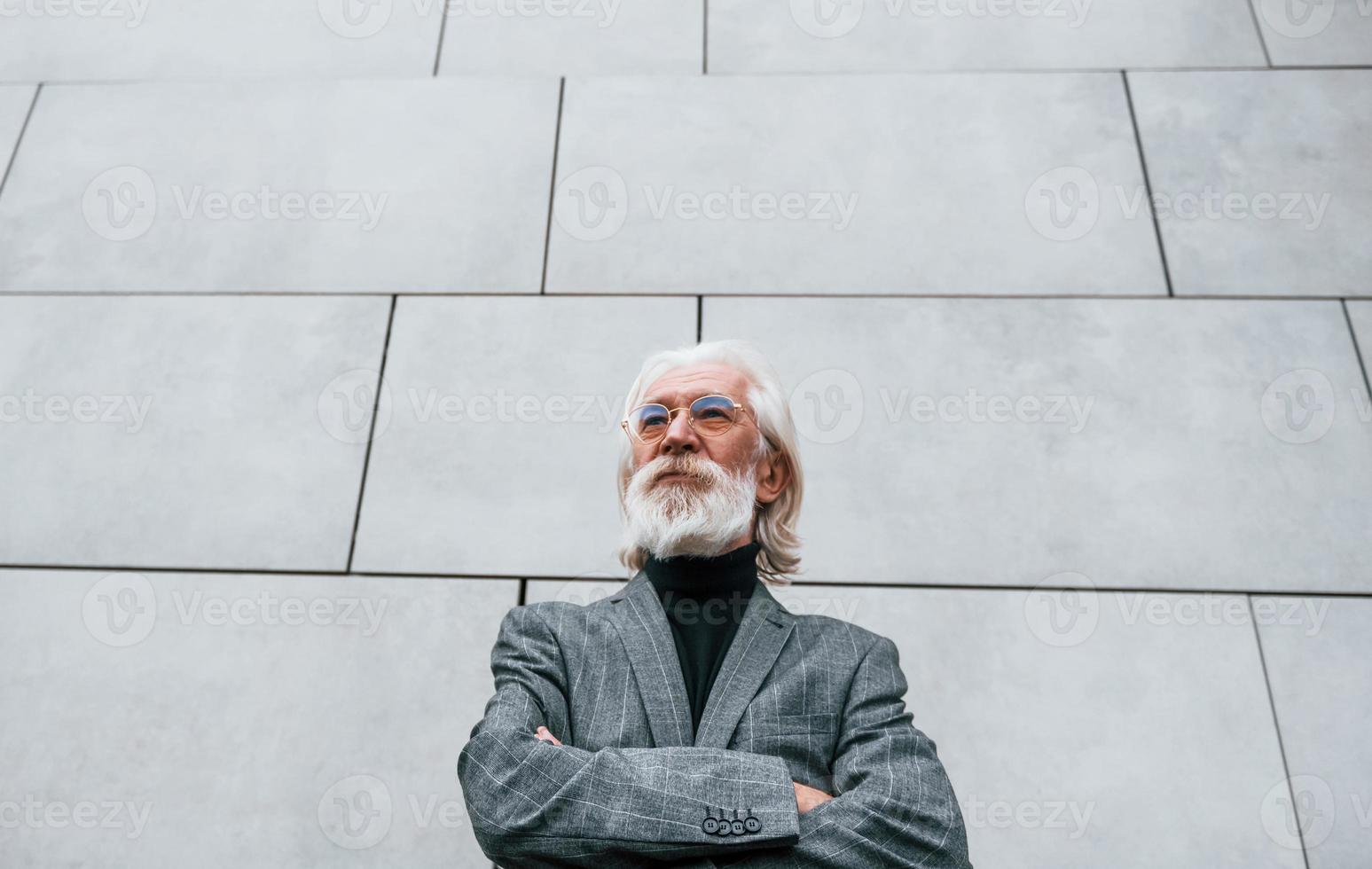 un hombre de negocios de alto rango vestido con ropa formal, con cabello gris y barba, está al aire libre parado contra la pared foto