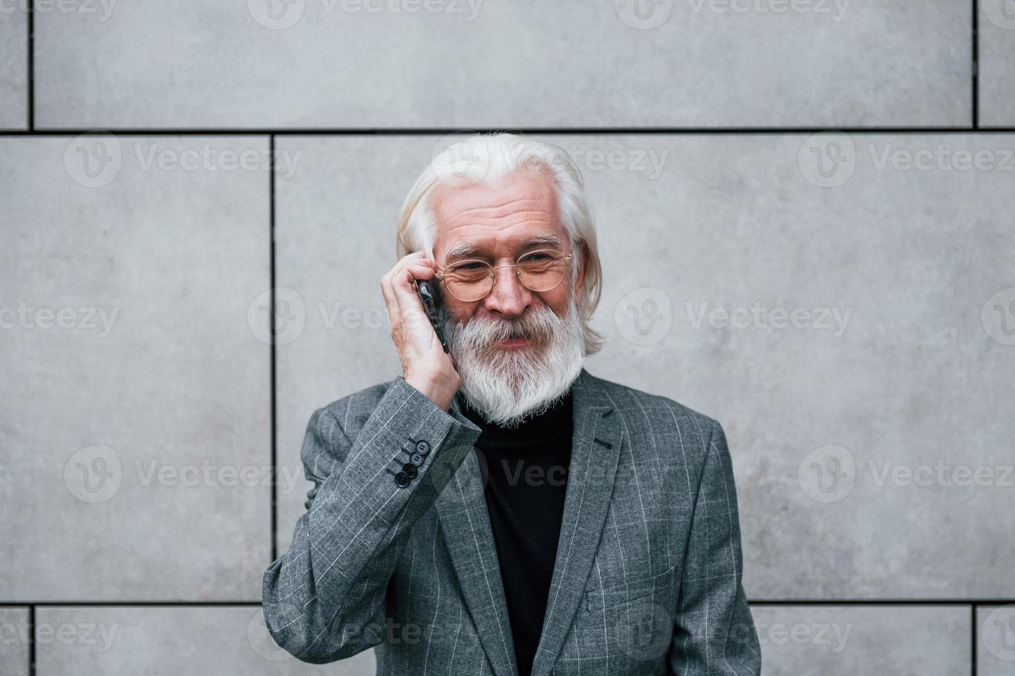 Senior businessman in formal clothes, with grey hair and beard is outdoors talks by phone photo