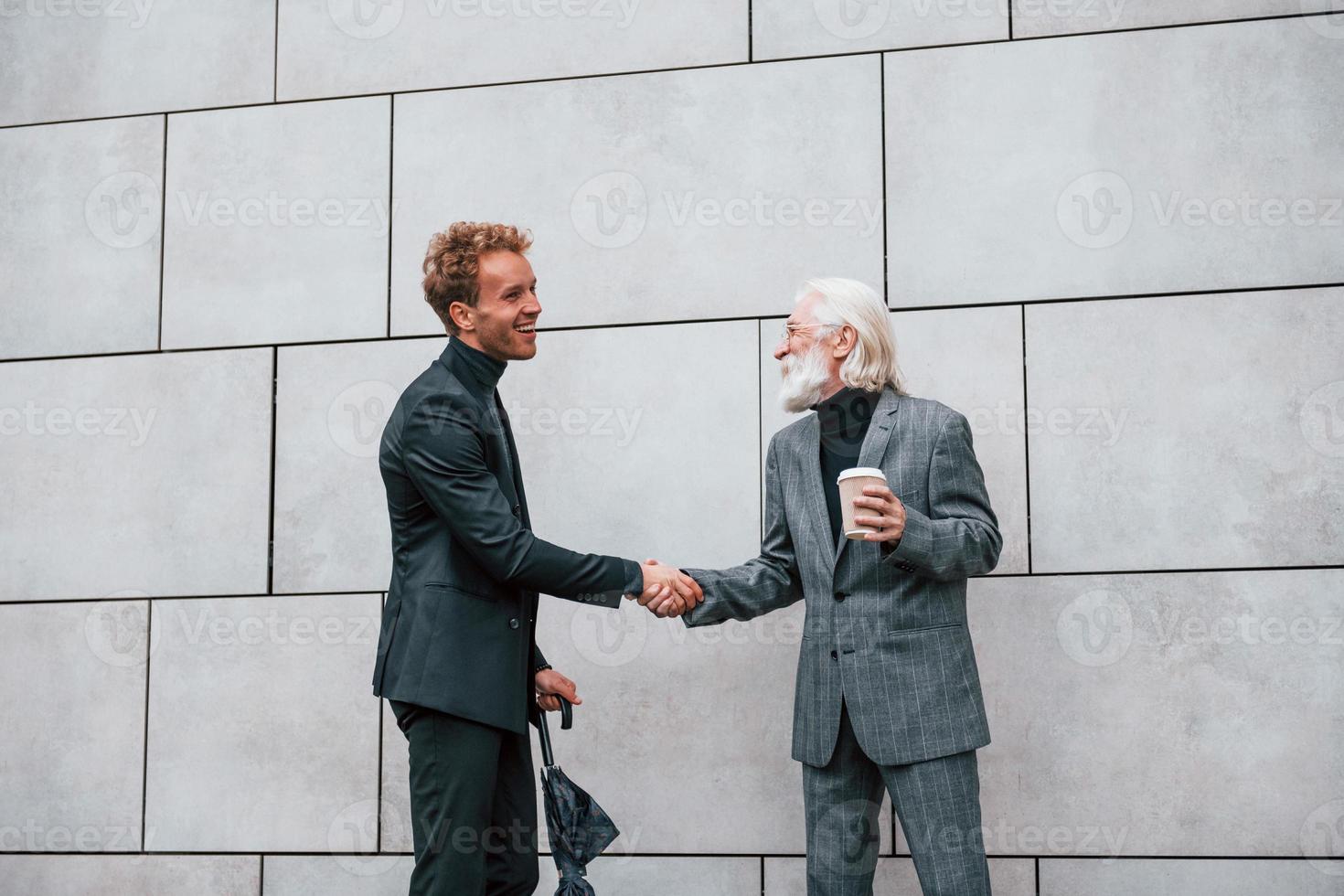 Having a meet. Young guy with senior man in elegant clothes is outdoors together. Conception of business photo