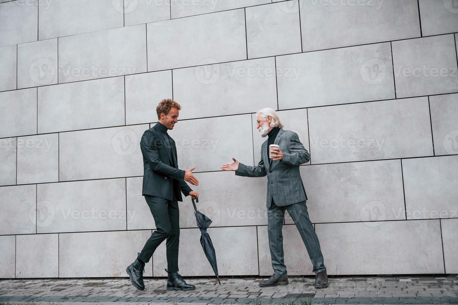 Having a meet. Young guy with senior man in elegant clothes is outdoors together. Conception of business photo