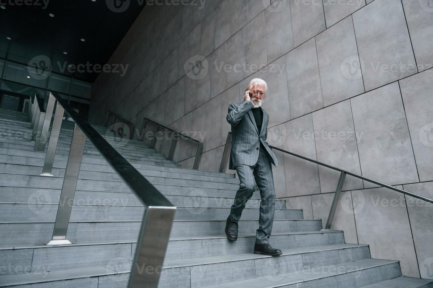 Senior businessman in formal clothes, with grey hair and beard is outdoors talks by phone photo