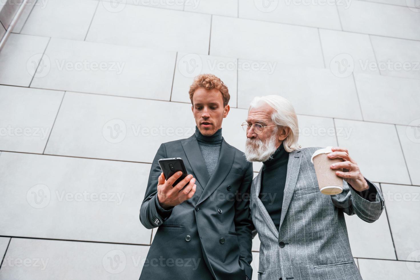 Young guy with senior man in elegant clothes is outdoors together. Conception of business photo