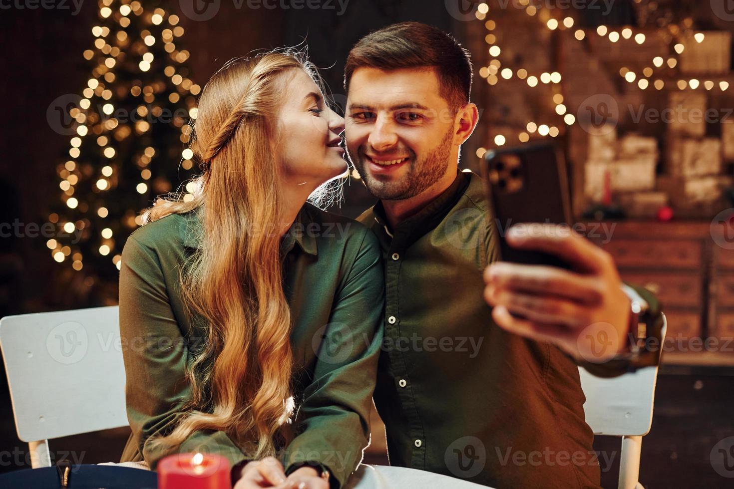 Making selfie by using phone. Young lovely couple have romantic dinner indoors together photo