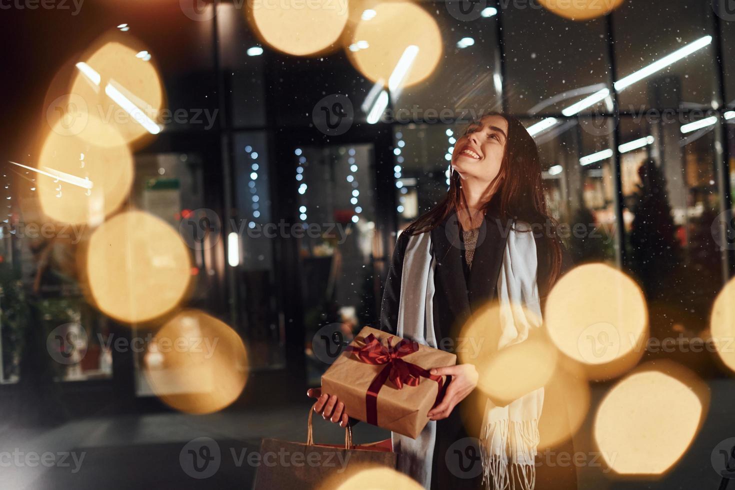 From the shop with gift box in hands. Cheerful woman is outdoors at Christmas holidays time. Conception of new year photo